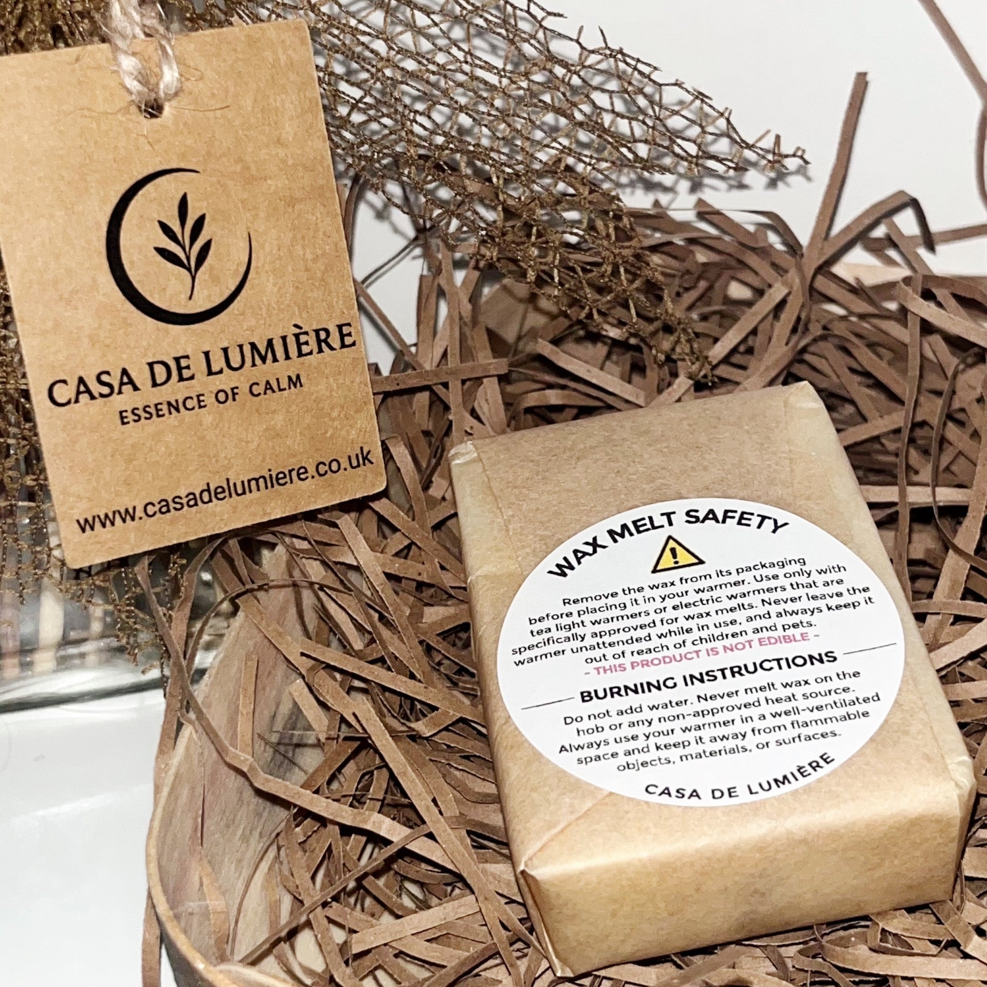Casa De Lumière eco-luxury wax melt bar wrapped in sustainable kraft paper with safety label, displayed on natural paper shred. Hand-poured in Cheshire, UK.